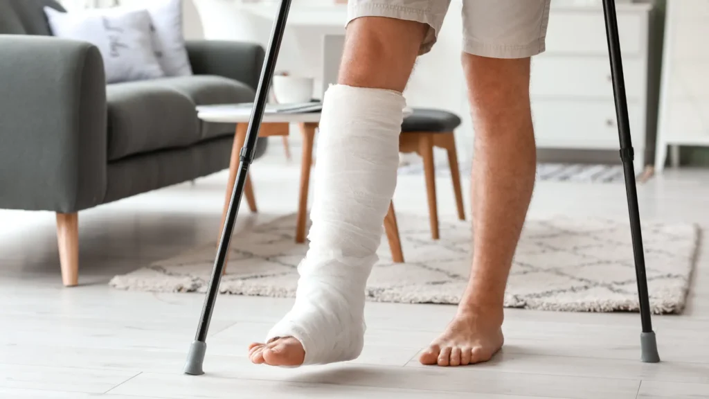 Mann mit Gips am Bein, gestützt von zwei Stöcken, im Wohnzimmer stehend