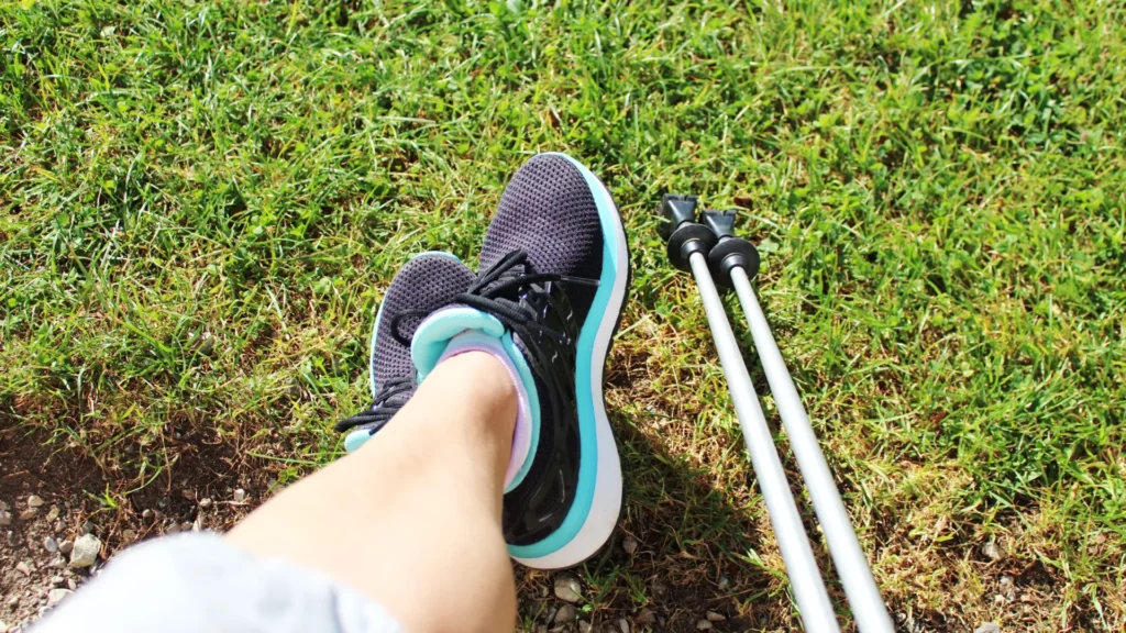 Nordic Walking Stöcke und Schuhe neben menschlichen Beinen, die auf eine Wiese zeigen